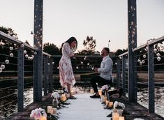 a man kneeling down next to a woman on a pier with candles in front of her