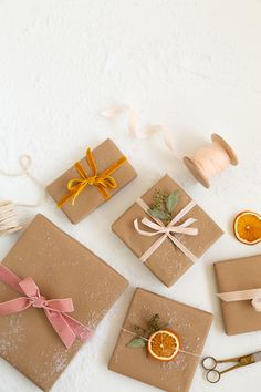 four wrapped presents with ribbons and orange slices on them, sitting next to some scissors