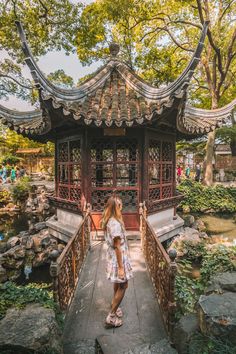 a woman standing on a bridge in front of a gazebo at a chinese garden