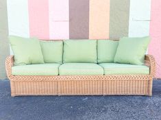 a wicker couch with green pillows in front of a colorful wall and striped wall