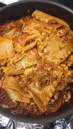 an iron skillet filled with pasta and meat covered in sauce on top of aluminum foil