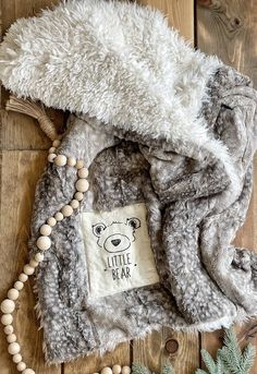 a teddy bear blanket and beads on a wooden floor next to a pine cone with the words little bear