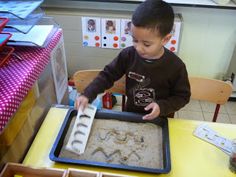 a little boy that is standing in front of a tray with some sand on it