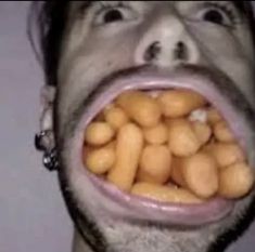 a man with his mouth open and peanuts coming out of his mouth to the side