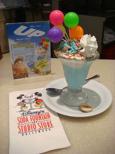 an ice cream sundae with sprinkles and balloons in it on a white plate