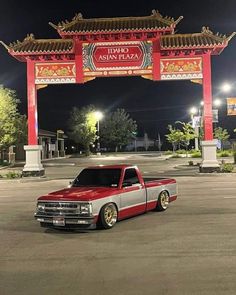 a red and white truck parked in front of a chinese archway at night with lights on