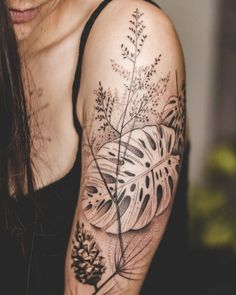 a woman with a black and white tattoo on her arm is holding a plant in front of her shoulder