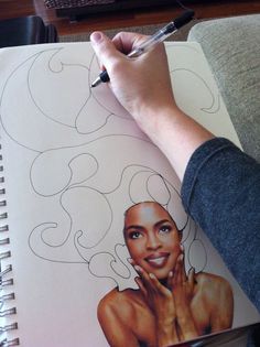 a person is holding a pen and drawing on a notebook with an image of a woman's face