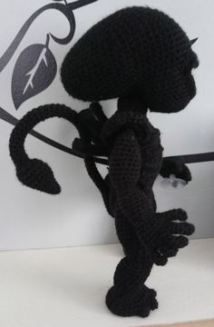 a crocheted black lizard holding onto a branch