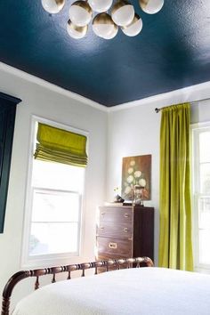 a bedroom with blue ceiling and green drapes on the window sill next to a dresser