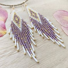 purple and white beaded fringe earrings on a wooden table next to pink flower petals