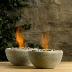 two stone bowls sitting on top of a wooden table next to a brick wall and fire