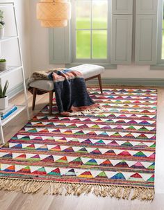 a multicolored rug with fringes on the floor in front of a window