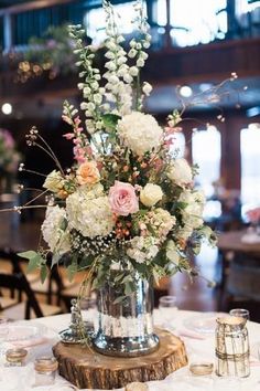 a vase filled with white and pink flowers on top of a wooden table next to other tables