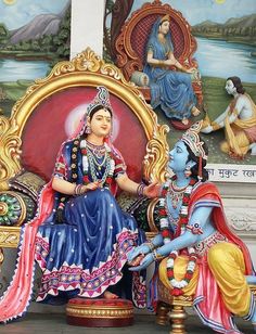 two statues of women sitting next to each other in front of a wall with paintings on it