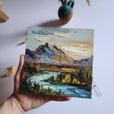 a person holding up a piece of art with mountains in the background and water below