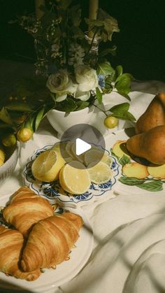 a table topped with croissants and fruit on top of a white cloth