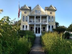 a large white house sitting in the middle of a lush green field next to bushes