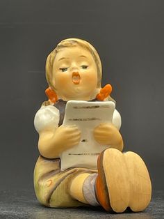 a ceramic figurine sitting on top of a table holding a tablet computer and looking at it