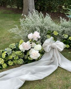 a wedding dress laying on the ground next to flowers and greenery in front of a tree