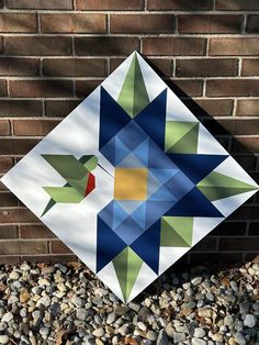 a colorful quilt sitting on top of a pile of rocks next to a brick wall