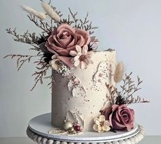 a white cake with pink flowers and feathers on it's side, sitting on a table