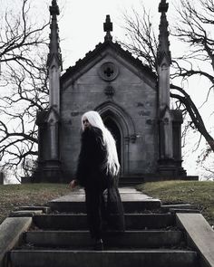 a woman with long white hair sitting on steps in front of an old stone church