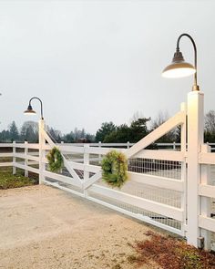 a white fence with wreaths on it and two lights hanging from the top one