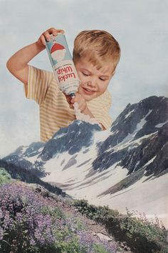 a young boy holding up a bottle of milk in front of a snowy mountain range