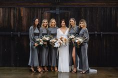 a group of women standing next to each other in front of a wooden wall holding bouquets