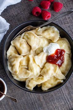 a bowl filled with dumplings and sauce next to raspberries on a table