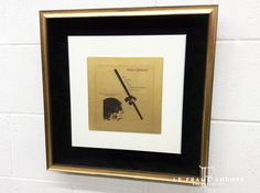 a black and gold framed print hanging on a white brick wall