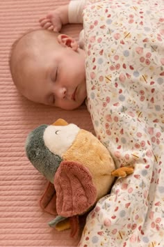 a baby sleeping next to a stuffed animal