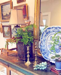 a table with plates and plants on it in front of a mirror, framed by pictures