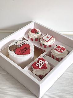 a box filled with lots of cupcakes covered in white frosting and red icing