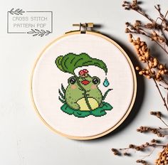 a cross stitch frog with a green hat on it's head