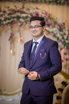 a man in a purple suit and tie standing next to a floral wall with flowers on it