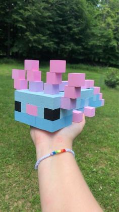 a hand holding up a small block toy in the shape of a cube with pink and blue blocks on it