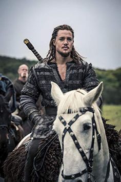 a man riding on the back of a white horse next to another man wearing armor