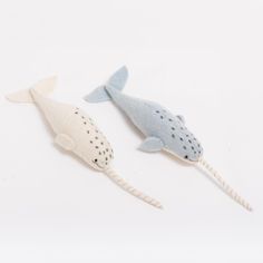 two stuffed whales are laying side by side on a white surface, one is gray and the other is light blue