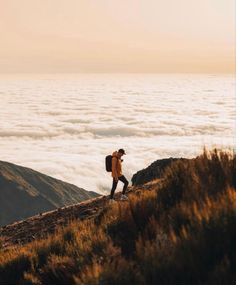 a man with a backpack walking up a hill above the clouds