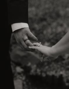 the bride and groom hold hands while holding each other's wedding rings in black and white