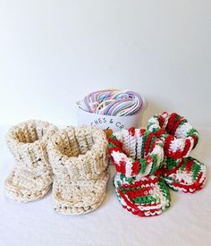 three crocheted baby booties sitting on top of a white table next to a bowl of yarn