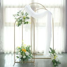 an arch decorated with flowers and greenery stands in front of a curtained window