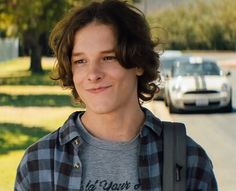 a young man is standing in front of some parked cars and looking at the camera