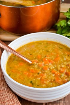 a bowl of soup with carrots and parsley on the side next to a pot