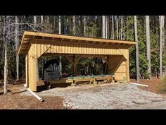 a wooden shelter in the middle of a forest with picnic tables and benches under it