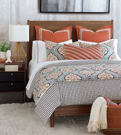 a bed with orange and white pillows on it next to a night stand, lamp and nightstand