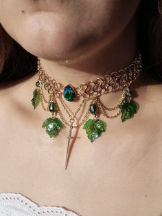 Behold the elegance of this gold-hued chainmail necklace! A vivid green rhinestone steals the spotlight at the heart, while a dangling sword charm and cascading layers of chains adorned with green teardrop beads and delicate ivy leaves add a touch of enchantment. Fit for a fairy warrior queen, this unique statement piece is destined to captivate. Actual colors of any item or chains may slightly differ from screen to screen due to the screen resolution. I take our pictures in natural light during Fairy Warrior, Chainmail Choker, Chainmail Necklace, Chunky Statement Necklace, Necklace Chunky, Funky Jewelry, Teardrop Beads, Fantasy Jewelry, Bijoux Diy