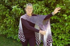 a woman is holding up a shawl in front of some bushes and trees with her hands out